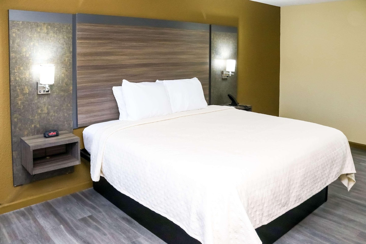 A hotel room with a large bed, two bedside tables, a nightstand, and wall-mounted lamps.