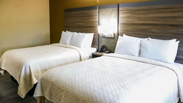 A hotel room with two beds, a nightstand, a lamp, and a wall-mounted light fixture. - Rodeway Inn Phenix City - Columbus (Phenix City)