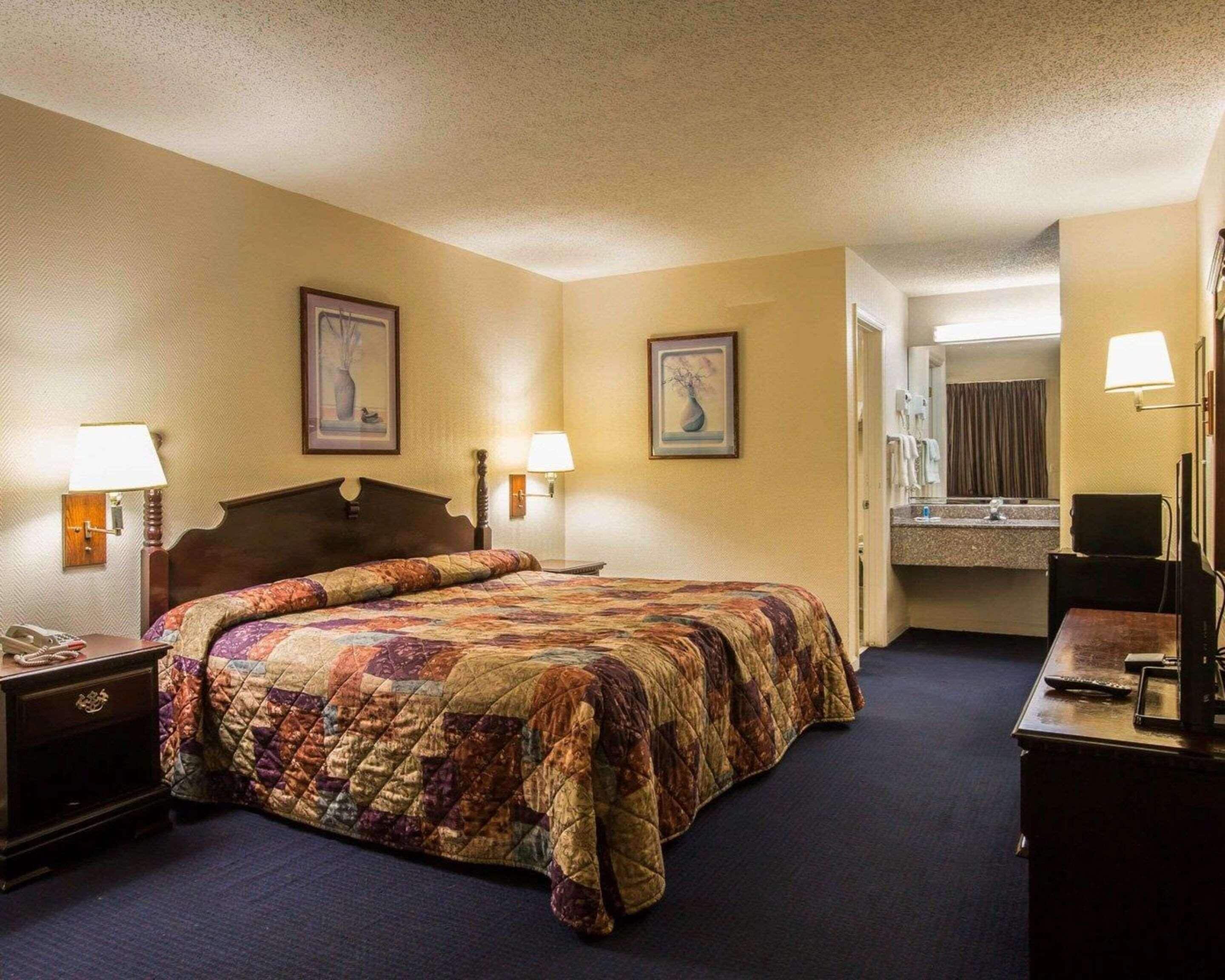 Ein Hotelzimmer mit einem großen Bett, zwei Nachttischlampen, einem Nachttisch, einem Schminktisch und einem durch eine offene Tür einsehbaren Badezimmer.