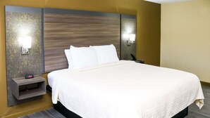 A hotel room with a large bed, two bedside tables, a wall-mounted phone, and two wall-mounted lights. - Rodeway Inn Phenix City - Columbus (Phenix City)