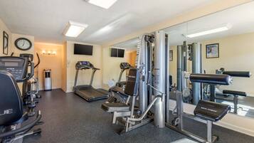 Ett hotells gym med löpband, styrketräningsmaskiner och en spegel.