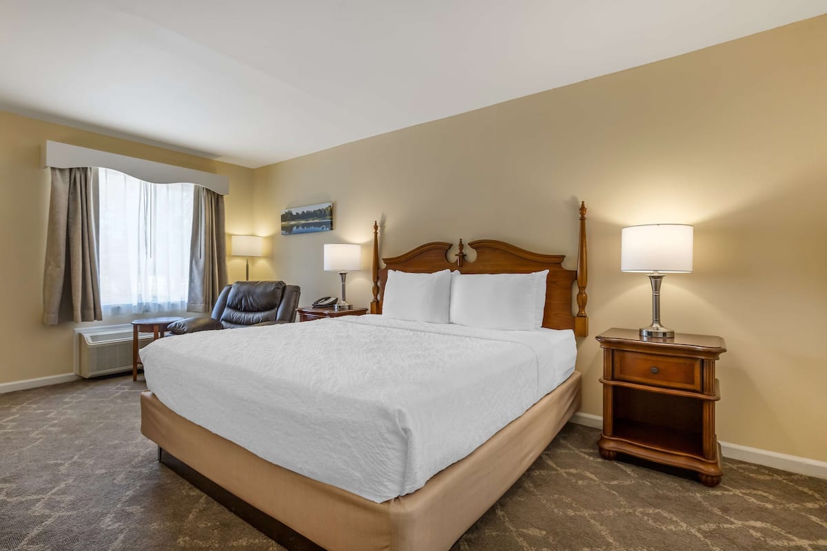 A hotel room with a large bed, two bedside tables with lamps, a chair, and a desk.