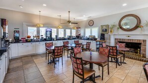 A spacious kitchen with white cabinets, a dining area with red patterned chairs, and a fireplace.