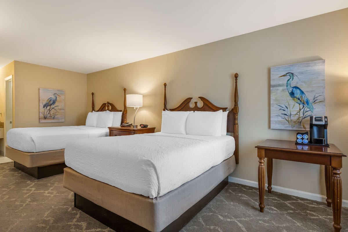 A hotel room with two beds, a coffee maker on a side table, and artwork on the walls.