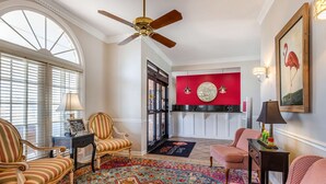 A spacious living room with a large window, a ceiling fan, and a vibrant red accent wall.