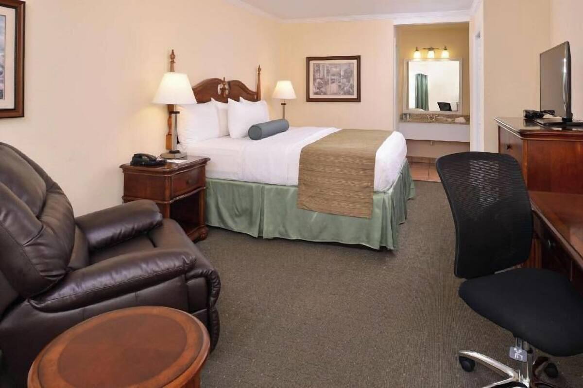 A hotel room with a bed, two bedside tables, a desk with a chair, a sofa, and a small round table.