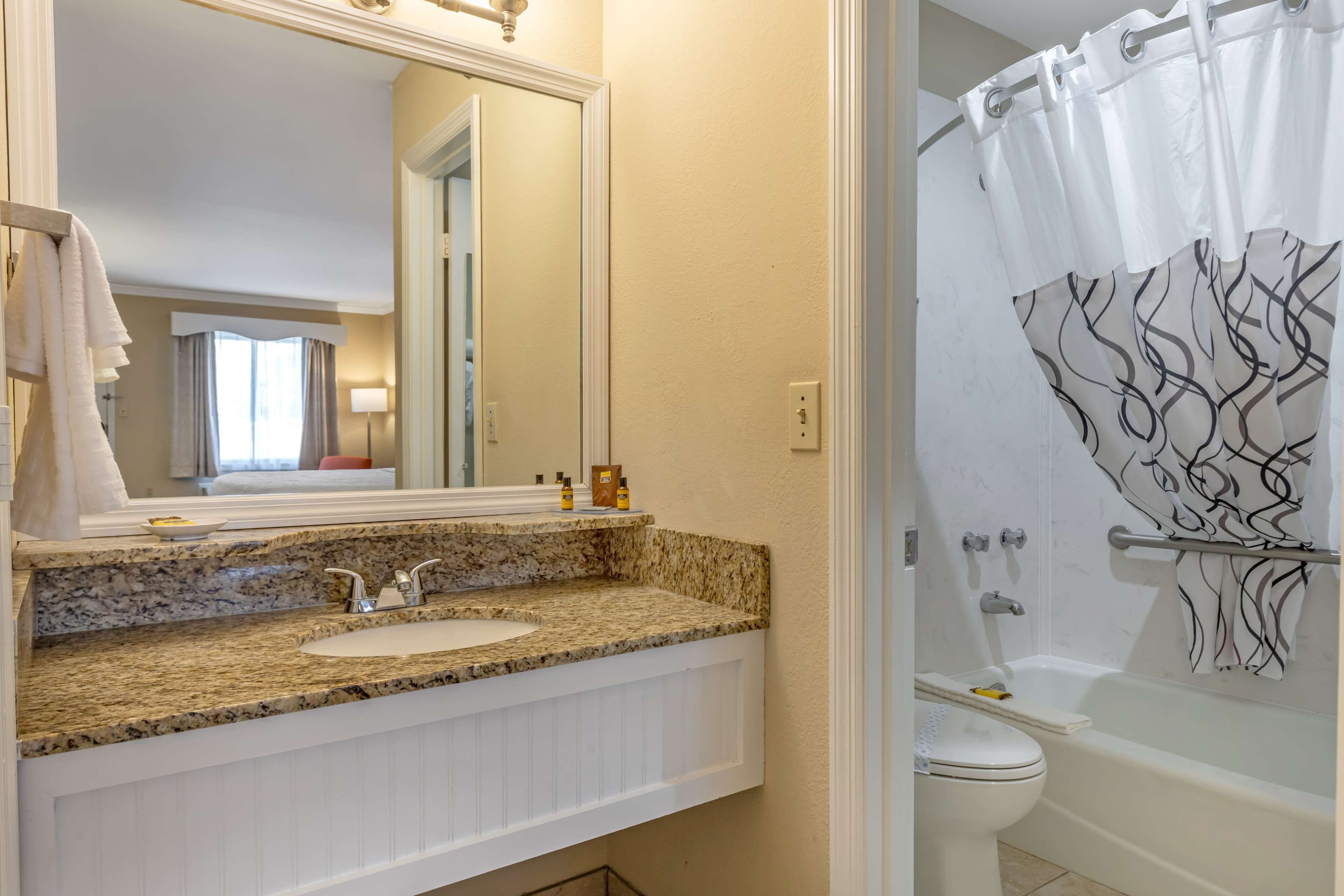 Un baño con encimera de granito, un lavabo blanco, un espejo, una ducha con cortina de diseño blanco y negro y un inodoro.