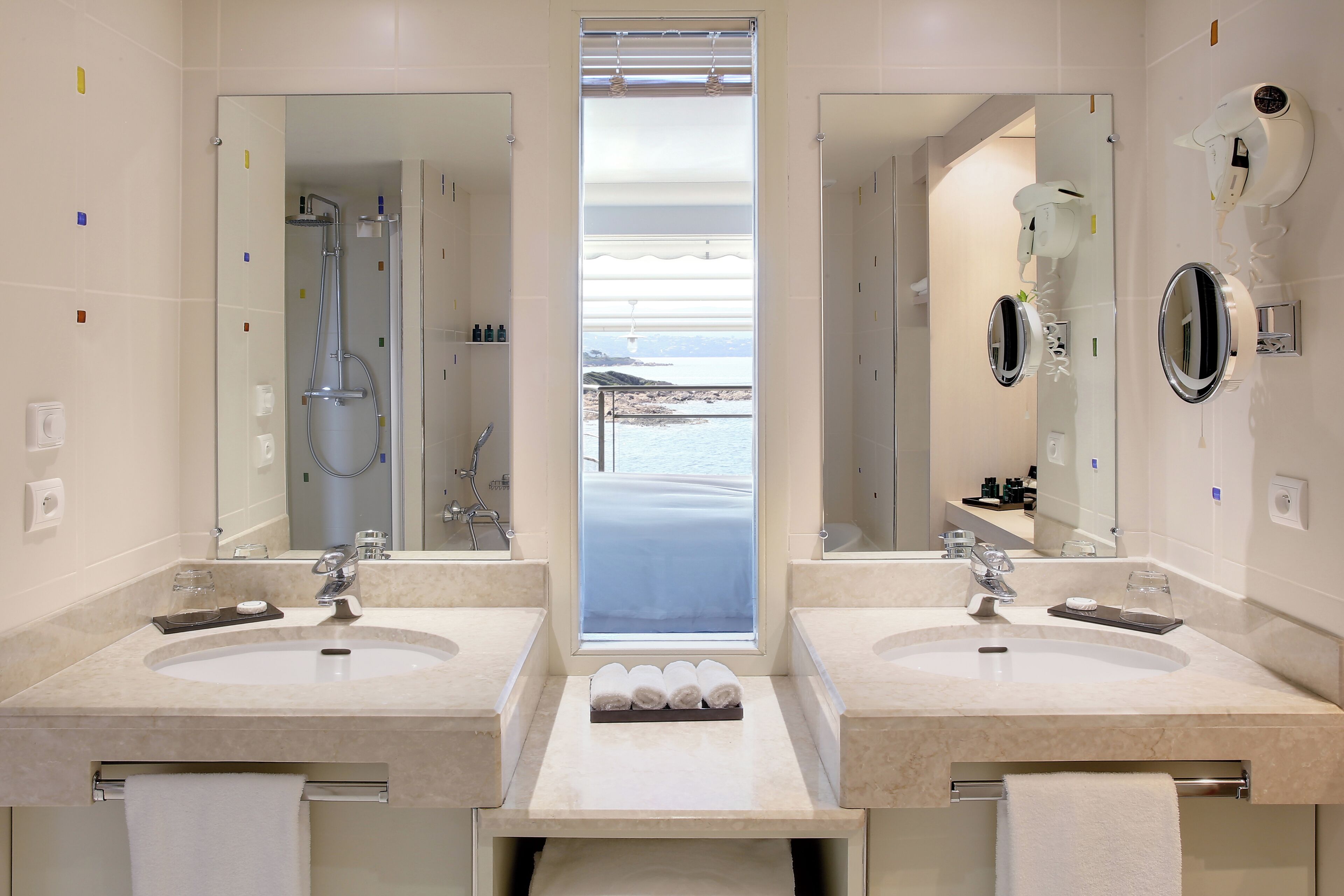 Un baño moderno con dos lavamanos, ducha y vistas al mar.