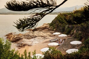 Una playa rocosa con sombrillas y sillas de playa blancas.