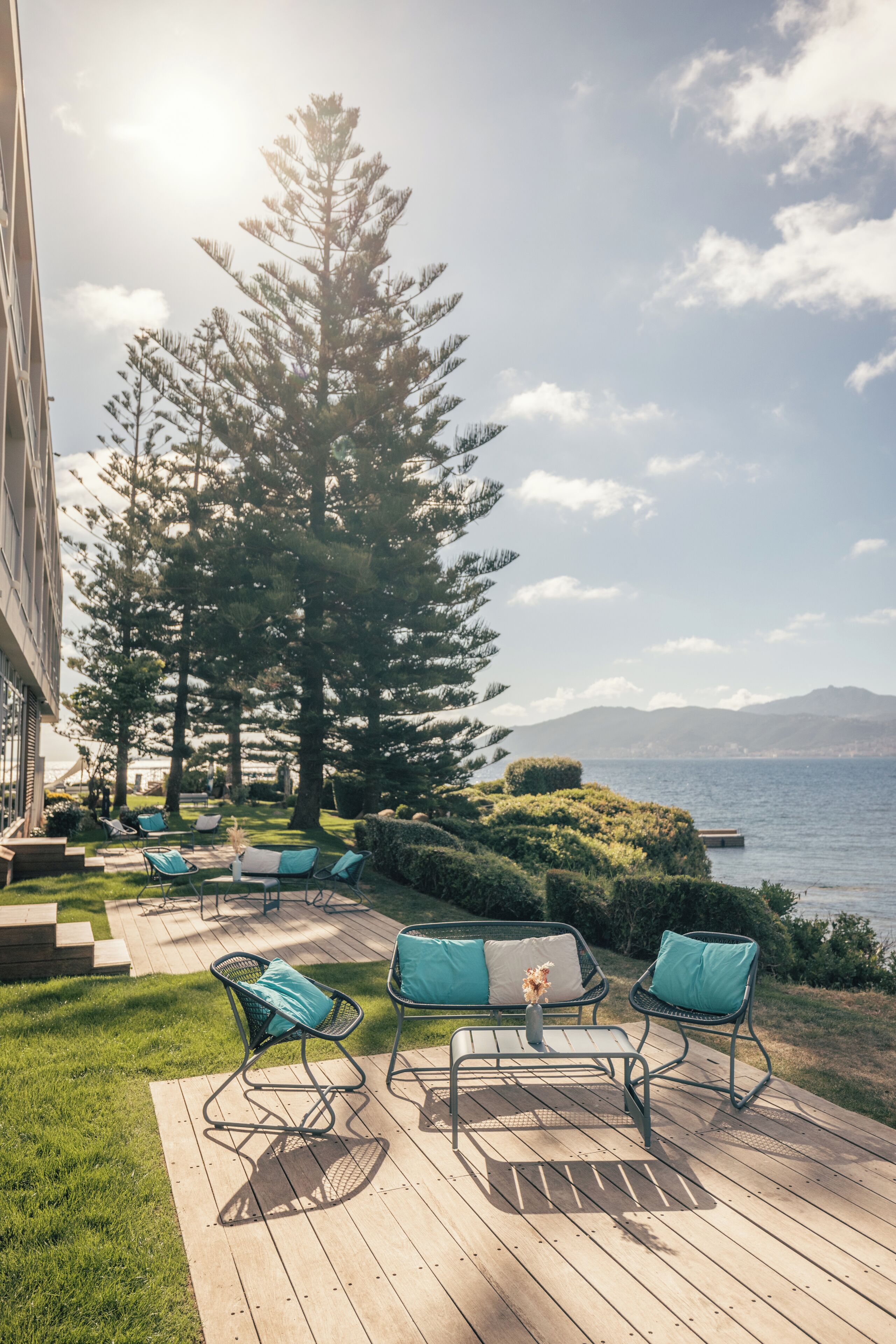 Une terrasse dotée de mobilier d’extérieur, offrant une vue sur la mer et abritant un grand arbre.