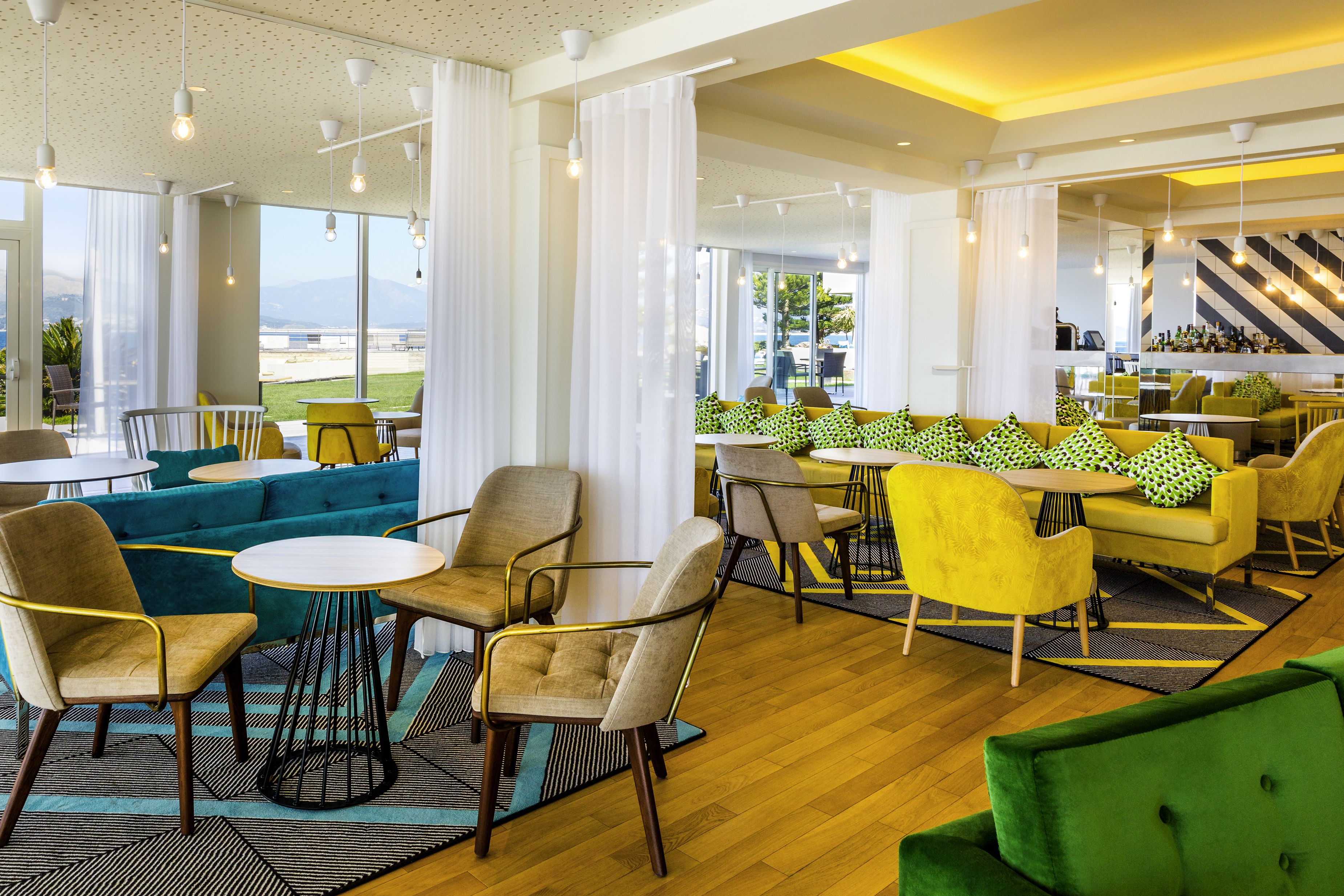 A modern lounge area with seating arrangements, large windows, and a view of the outdoors.