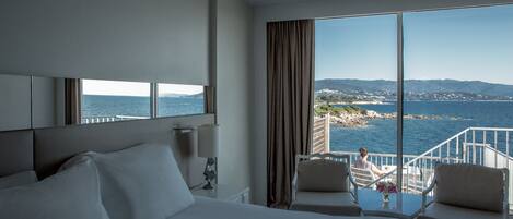 A hotel room with a large bed, a desk, and a view of the sea.