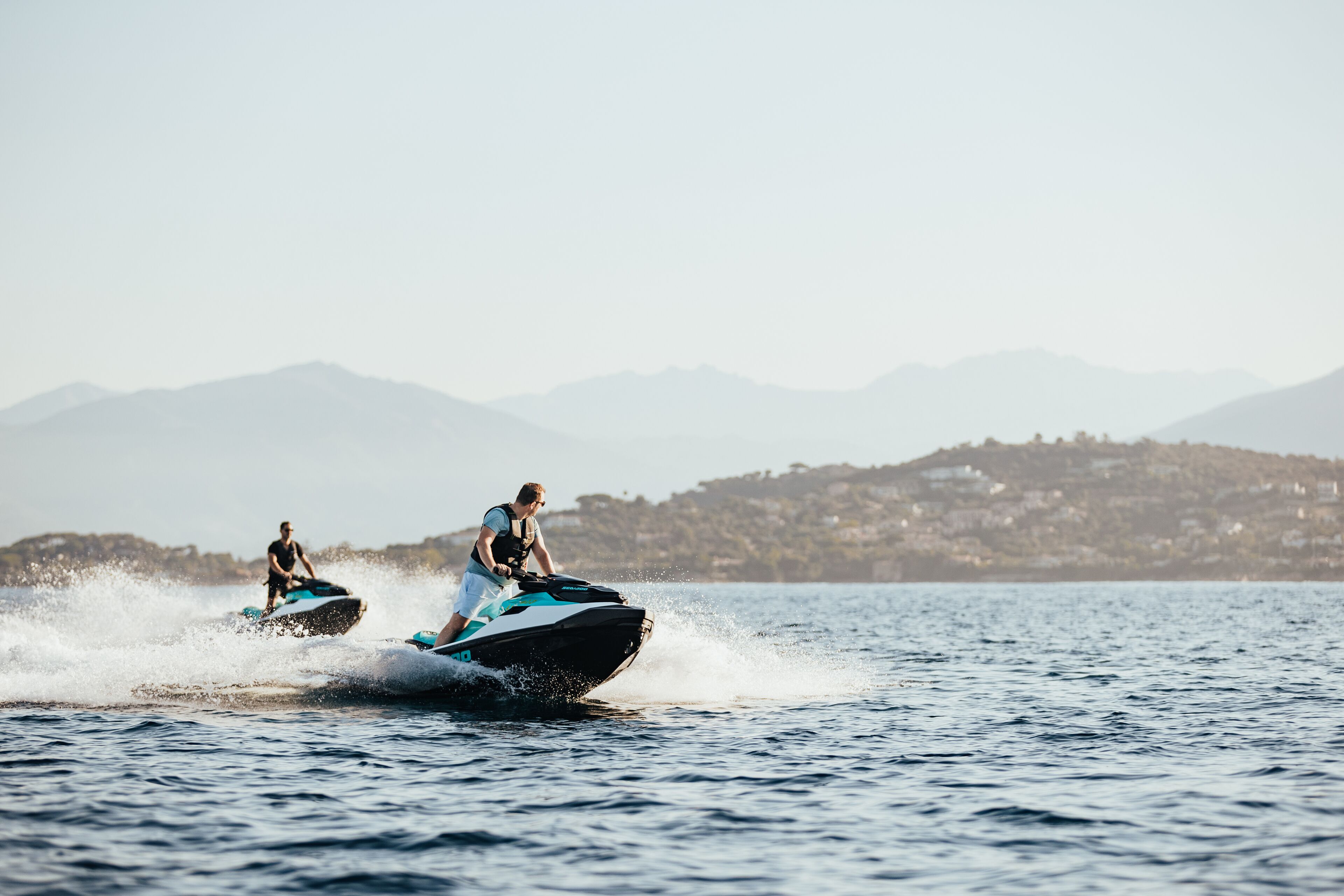 Two people jet-skiing on a lake with mountains in the background.