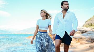 A couple walking on a beach with clear skies and calm waters.
