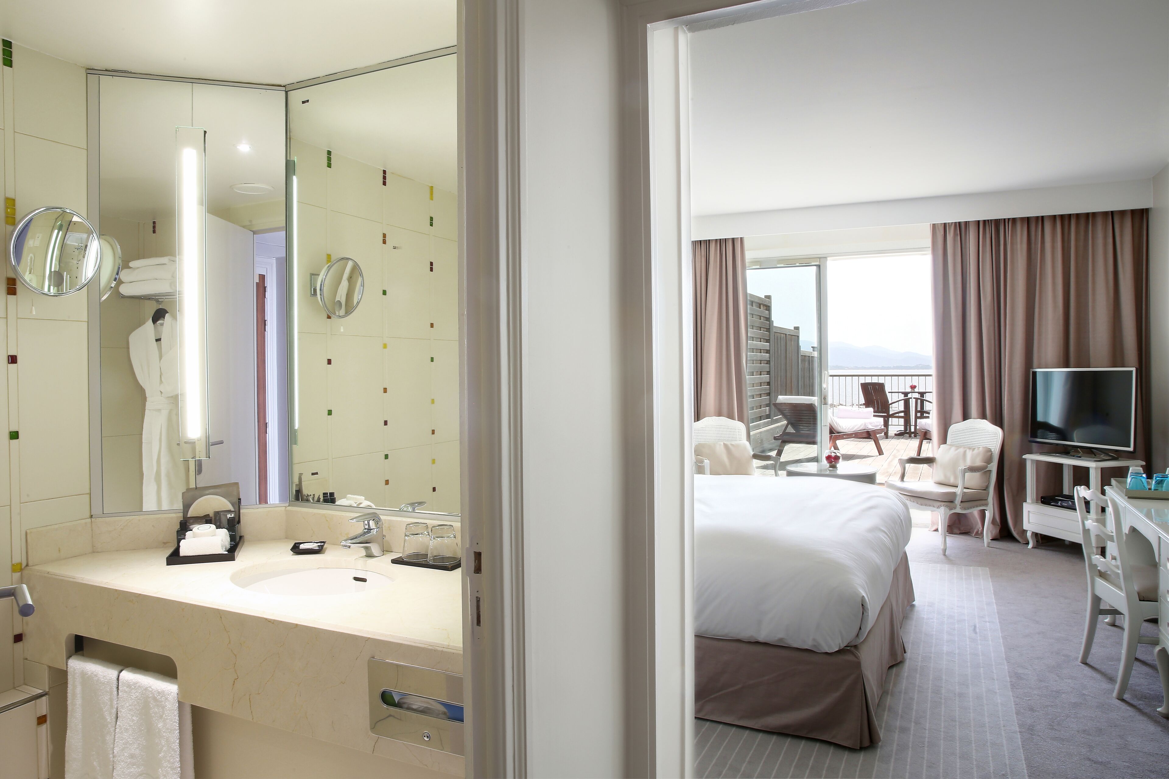 A hotel room with a large bed, a desk, a TV, and a bathroom with a mirror and sink.