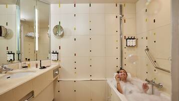 A bathroom with a bathtub, a sink, and a mirror. There are toiletries on the wall and a towel rack.
