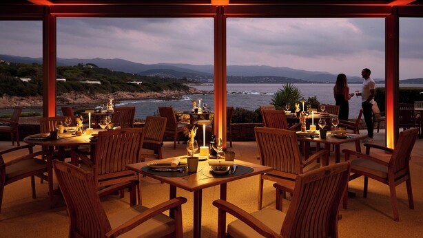 An outdoor dining area with wooden tables and chairs, overlooking a coastal landscape. - Sofitel Golfe Ajaccio Thalassa Sea & Spa (Grosseto-Prugna)