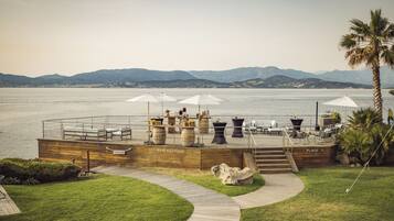 A waterfront terrace with outdoor seating, a wooden deck, and a view of the sea and mountains.