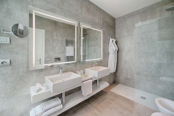 A modern bathroom with two sinks, a large mirror, a glass shower enclosure, and a white bathtub.
