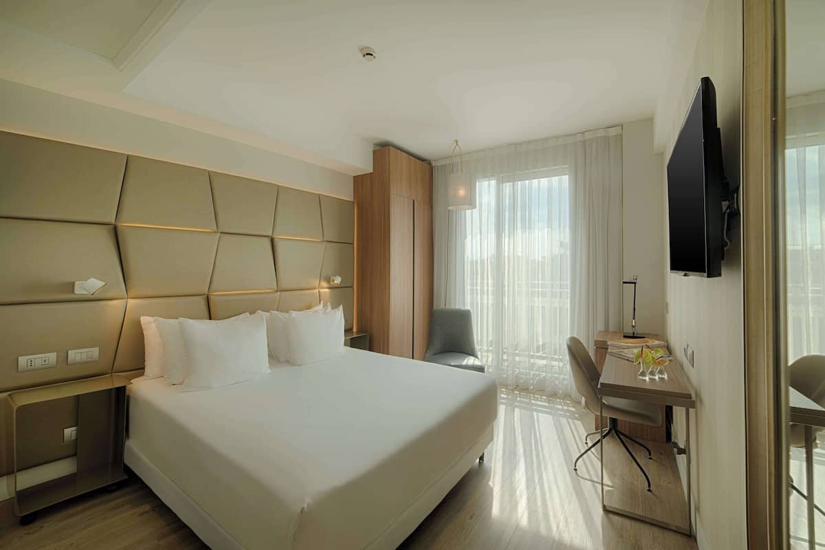 A modern hotel room with a large bed, a desk, and a television.