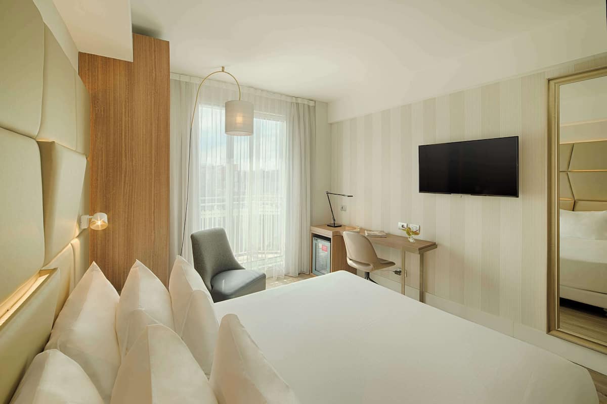 A hotel room with a large bed, a desk, a chair, a TV, and a mirror.