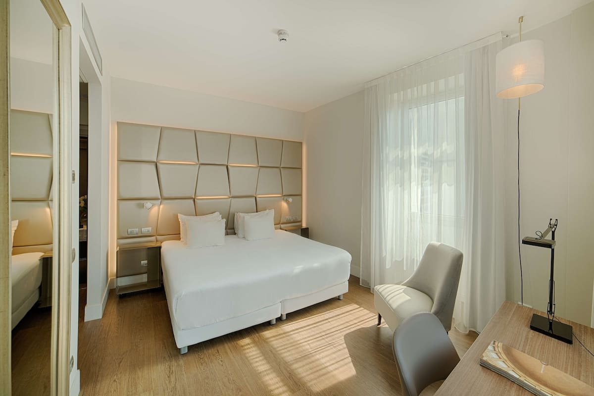 A modern hotel room with a large bed, a chair, a desk, and a lamp.