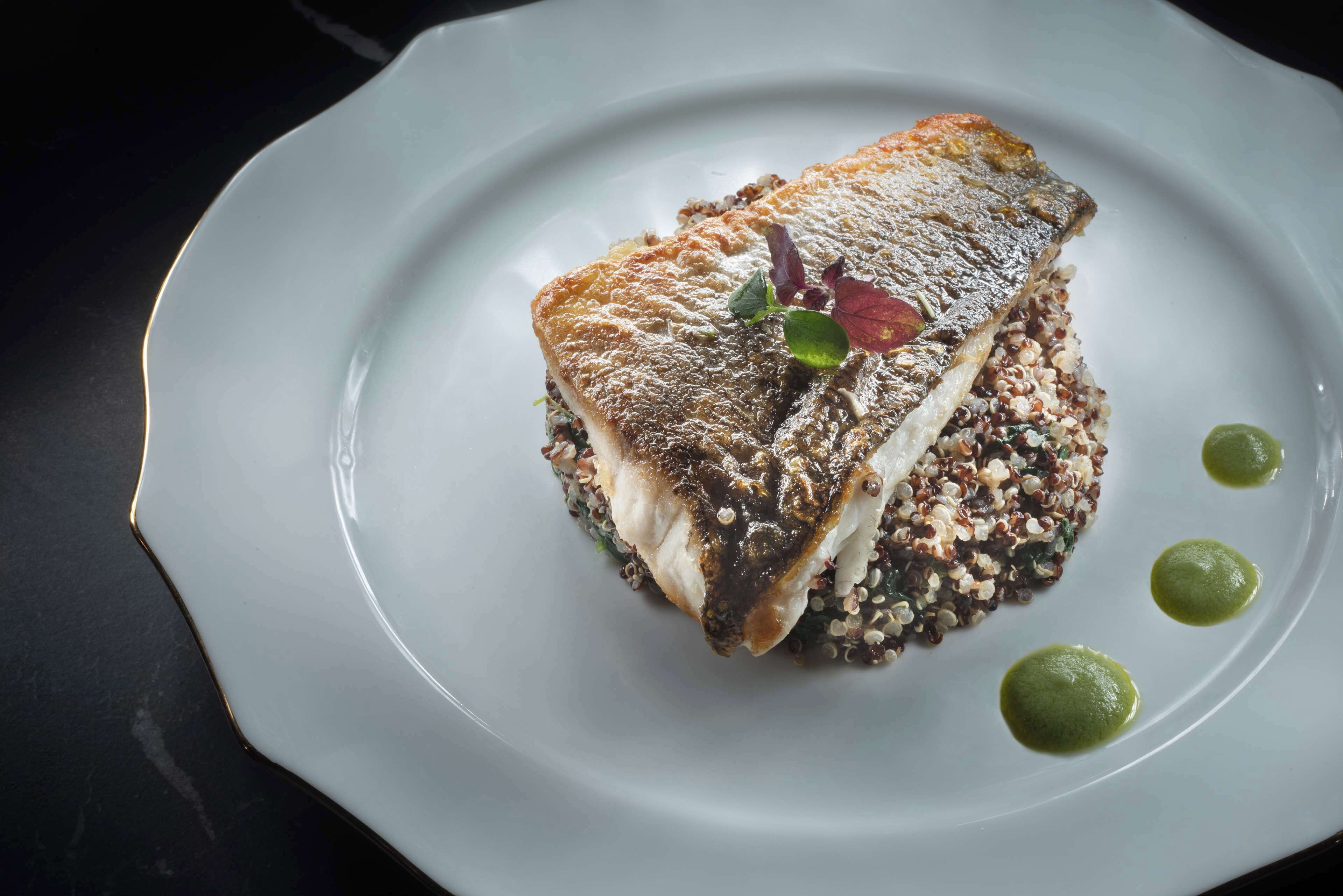 Un plato blanco con un trozo de pescado, quinua y salsa verde.