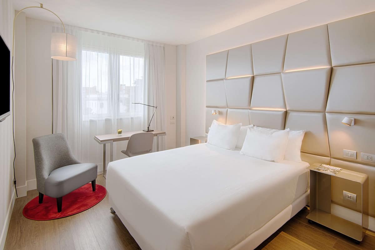 A modern hotel room with a large bed, a desk, and a chair.