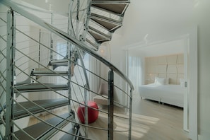 A modern interior with a spiral staircase, a bed with a headboard, and a red ottoman.