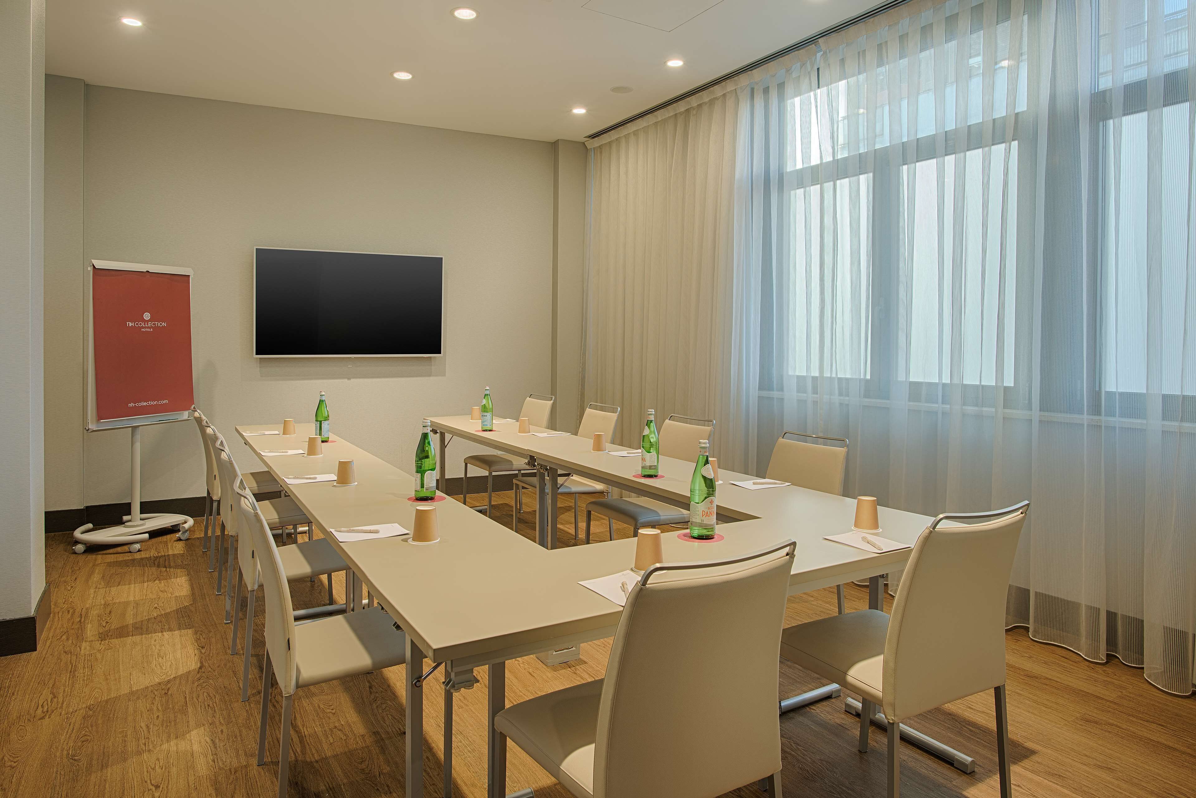 A conference room with a long table, chairs, a projector screen, and a large window with sheer curtains.