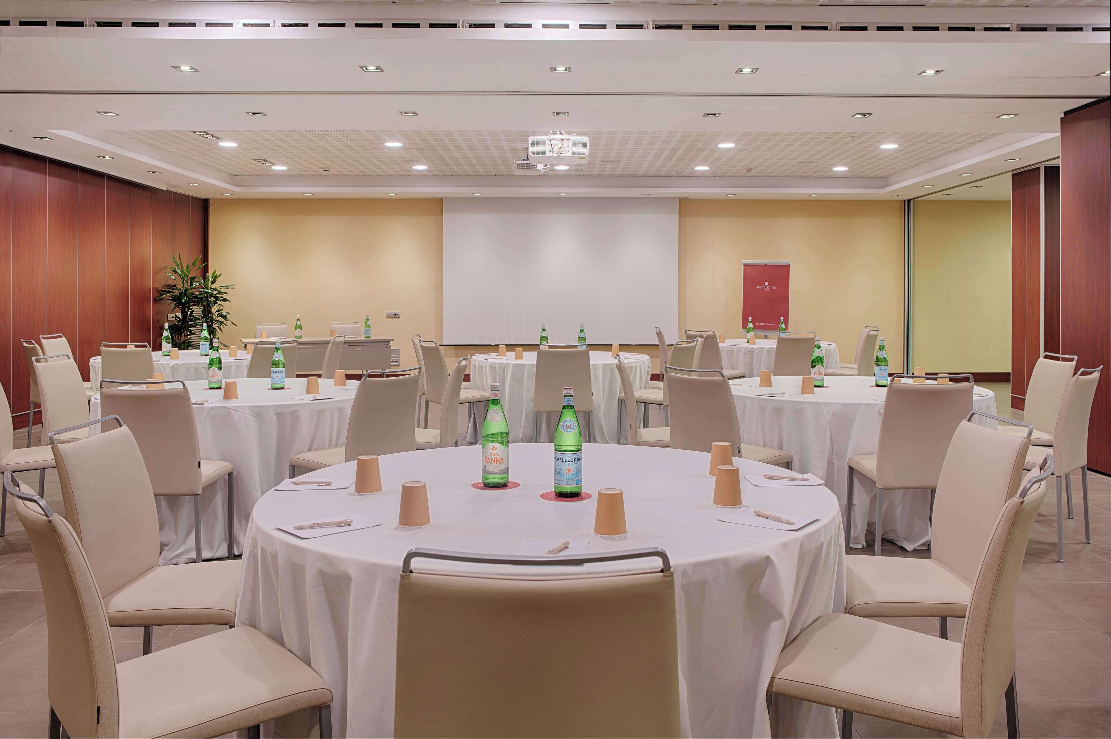 A conference room with multiple round tables, each with chairs, white tablecloths, and water bottles.