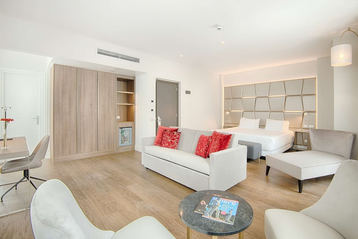 A modern hotel room with a bed, sofa, armchair, and a small table with a magazine.