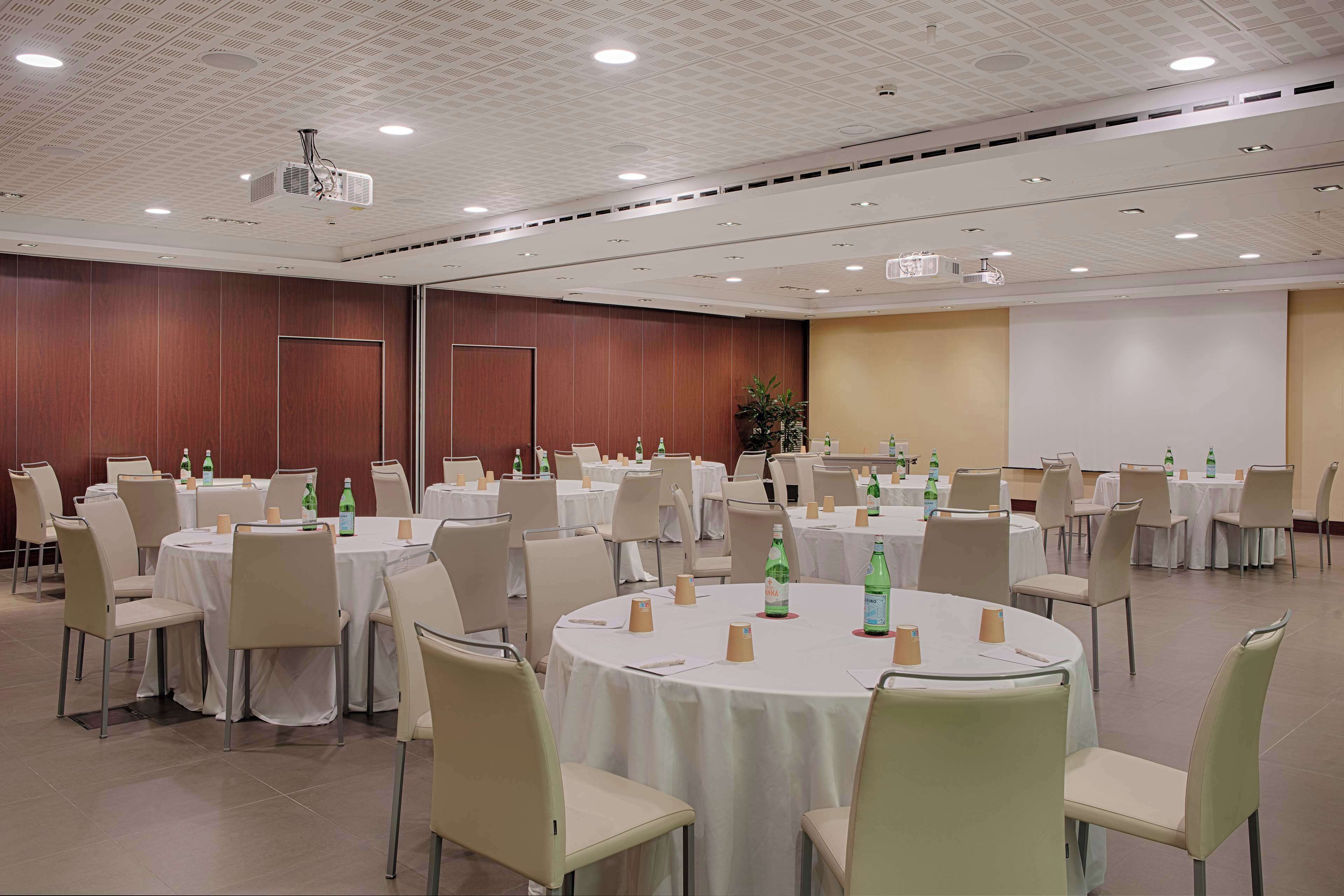 A conference room with round tables, chairs, and a projector screen.