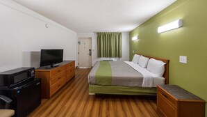 Egy szállodai szoba, amelyben található egy ágy, egy televízió, egy íróasztal mikrohullámú sütővel, és egy zöld színű fal.