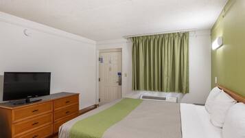 A hotel room with a bed, a TV on a wooden dresser, a green curtain, and a white door.
