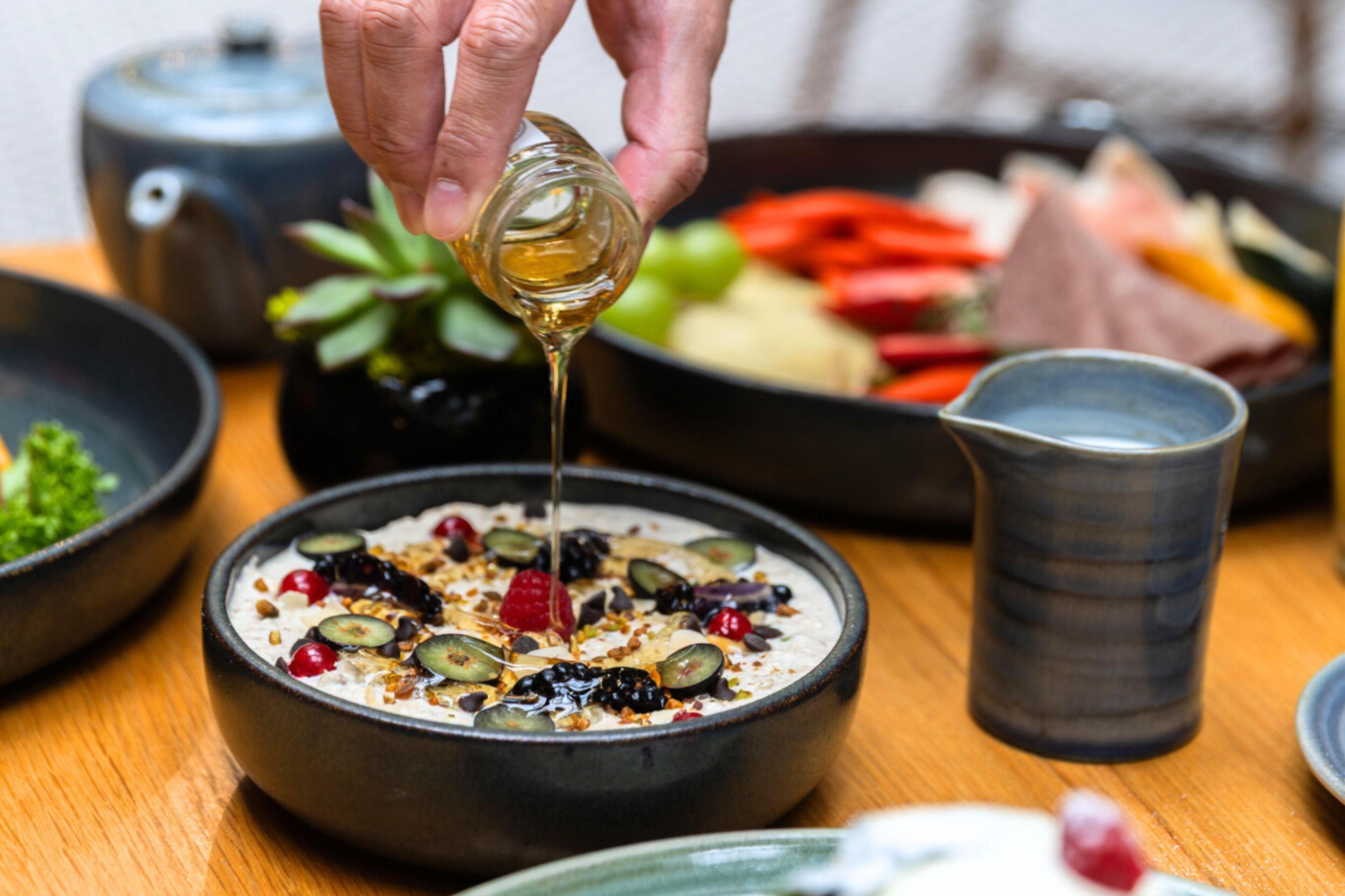En skål yoghurt toppet med frugt, og en hånd hælder sirup over.