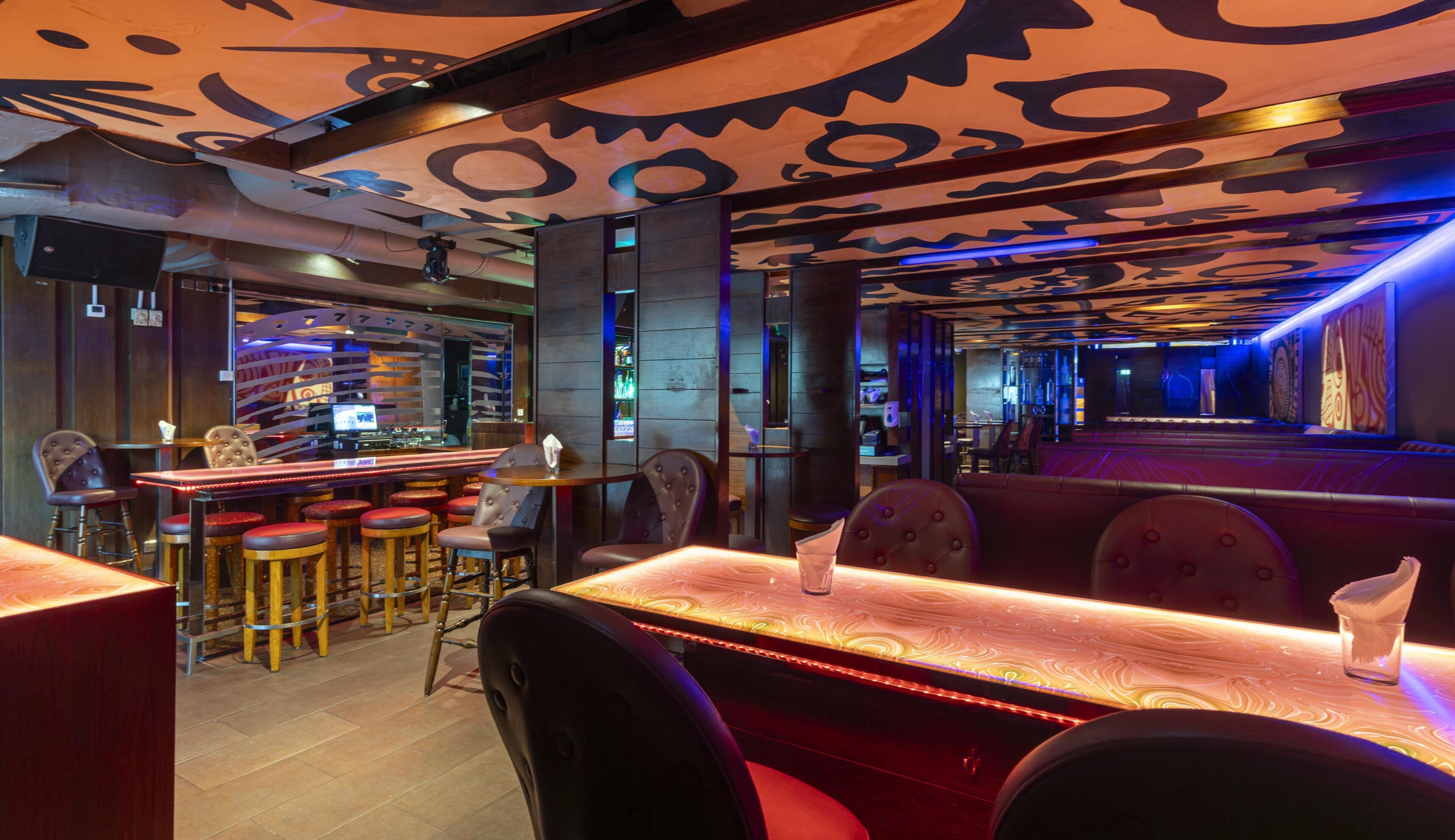 Eine Bar mit Hockern und einer Theke, ein Sitzbereich mit gepolsterten Nischen, sowie eine Musterdecke.