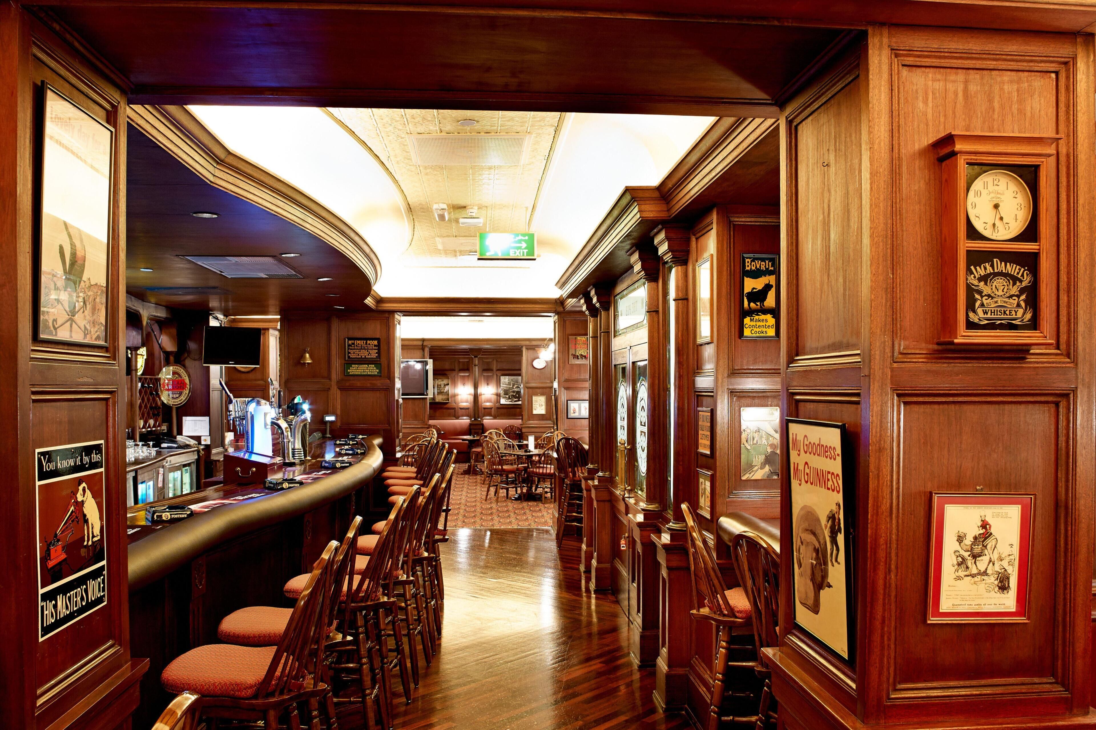 A bar area with wooden furnishings, a clock, and framed posters.