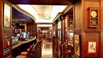 A bar area with wooden furnishings, a clock, and framed posters.