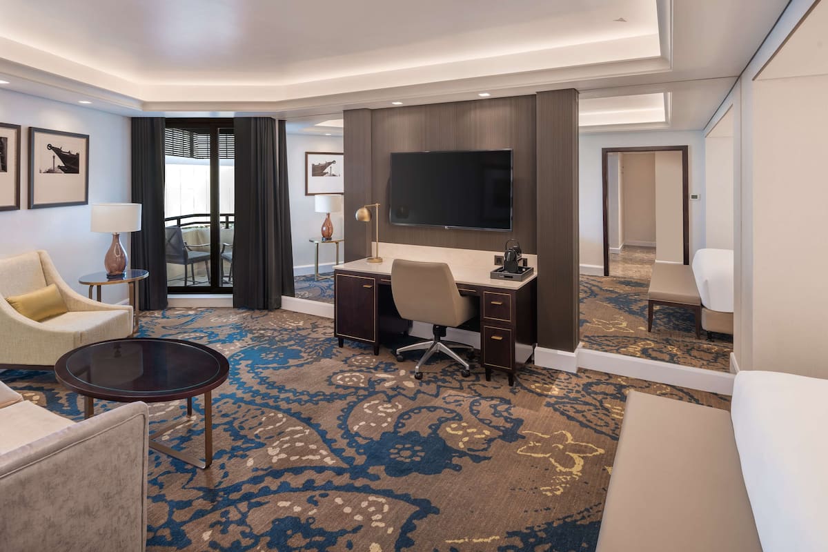 A hotel room with a desk, chair, sofa, and a TV.
