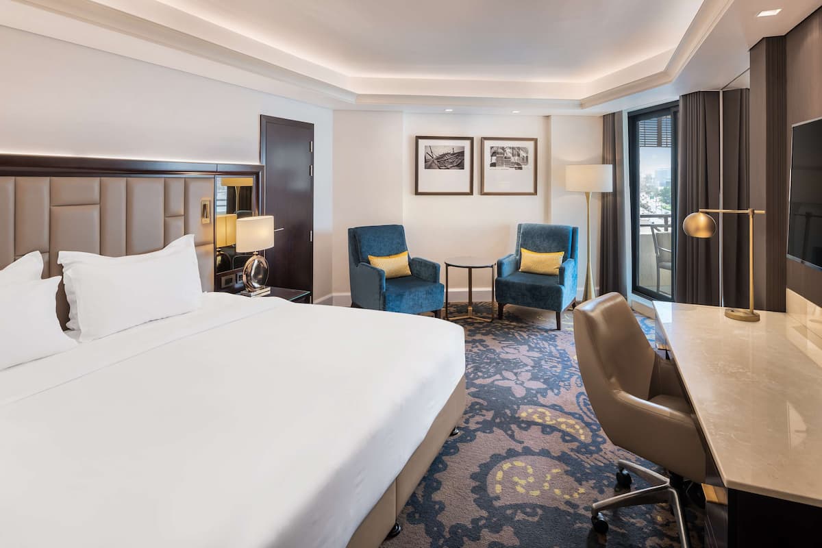 A hotel room with a large bed, two armchairs, a small table, and a desk with a chair.
