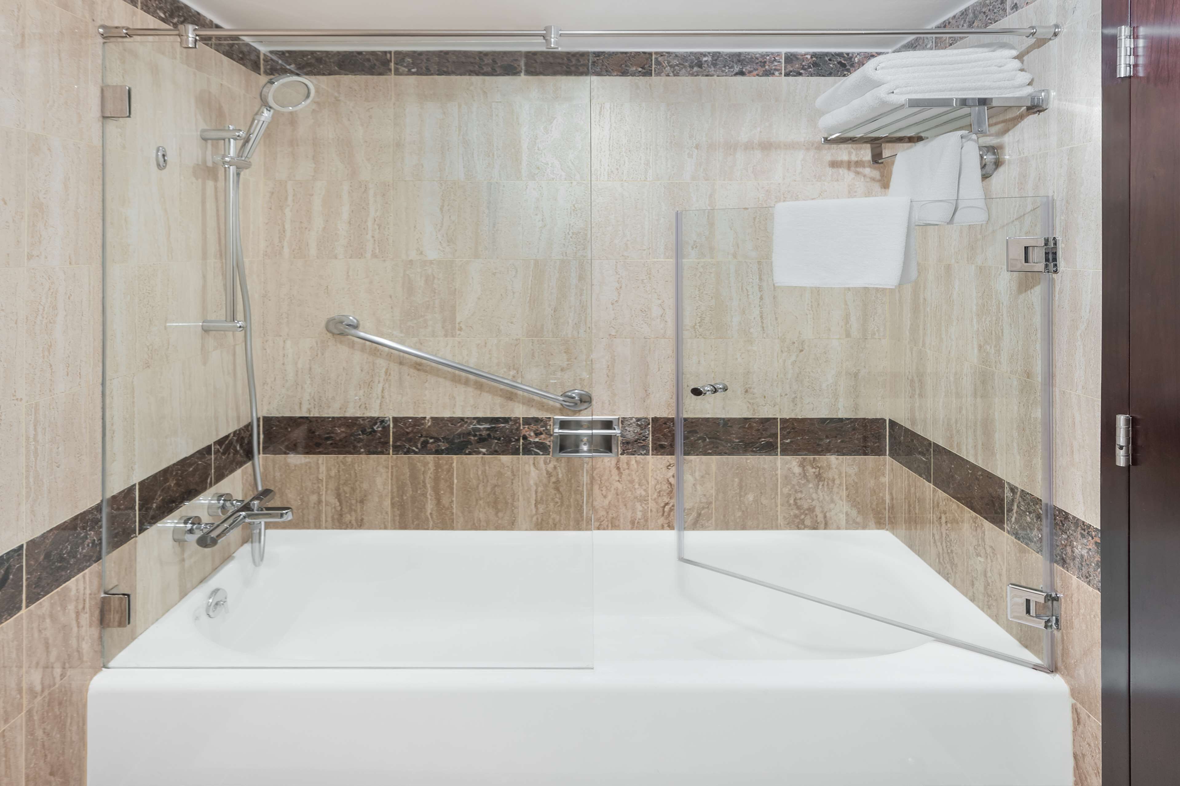 Un baño moderno con ducha envuelta en vidrio, una bañera blanca y un perchero con toallas dobladas.
