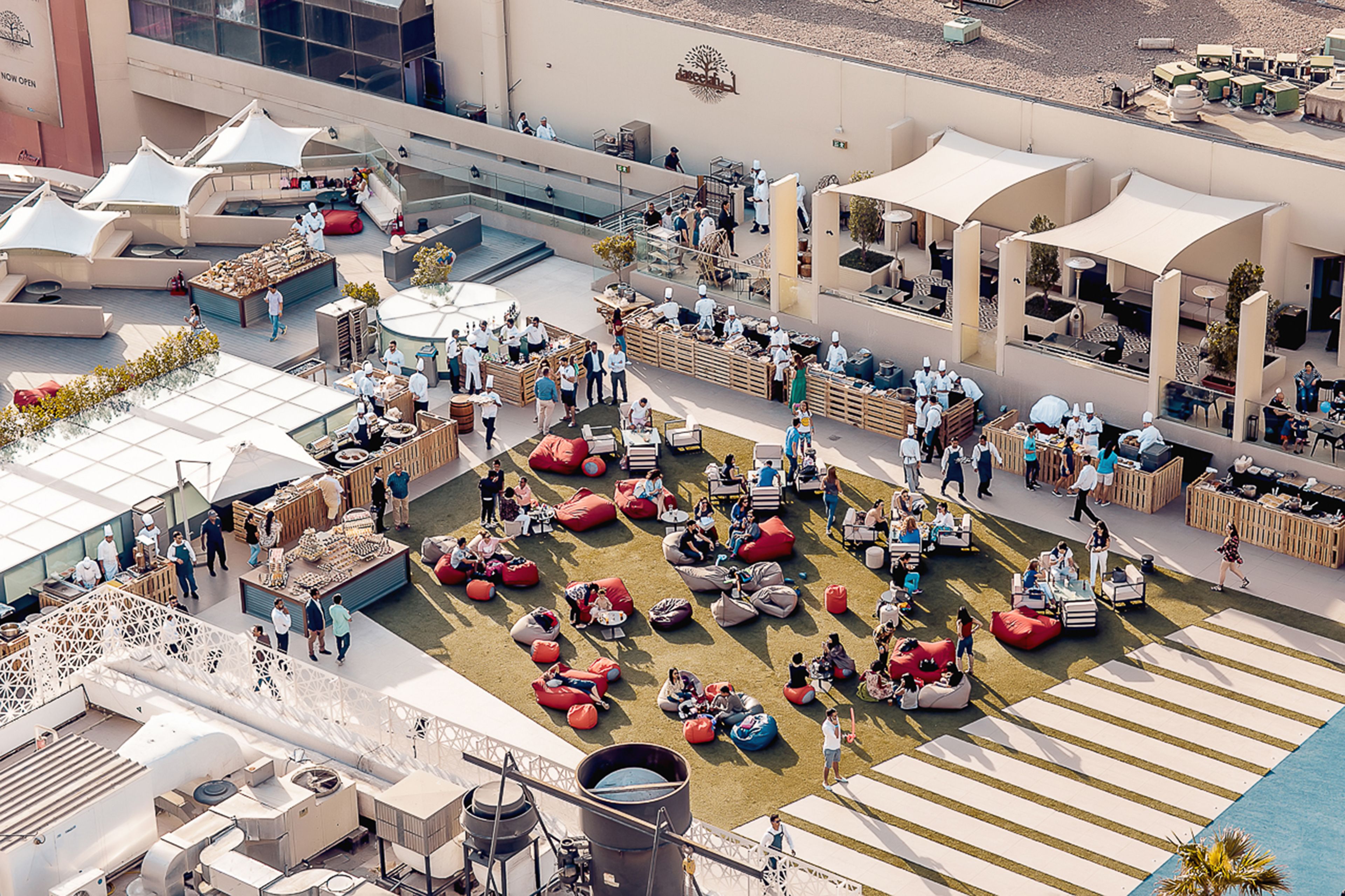Un espacio para eventos al aire libre con zonas de estar, mesas y un escenario.