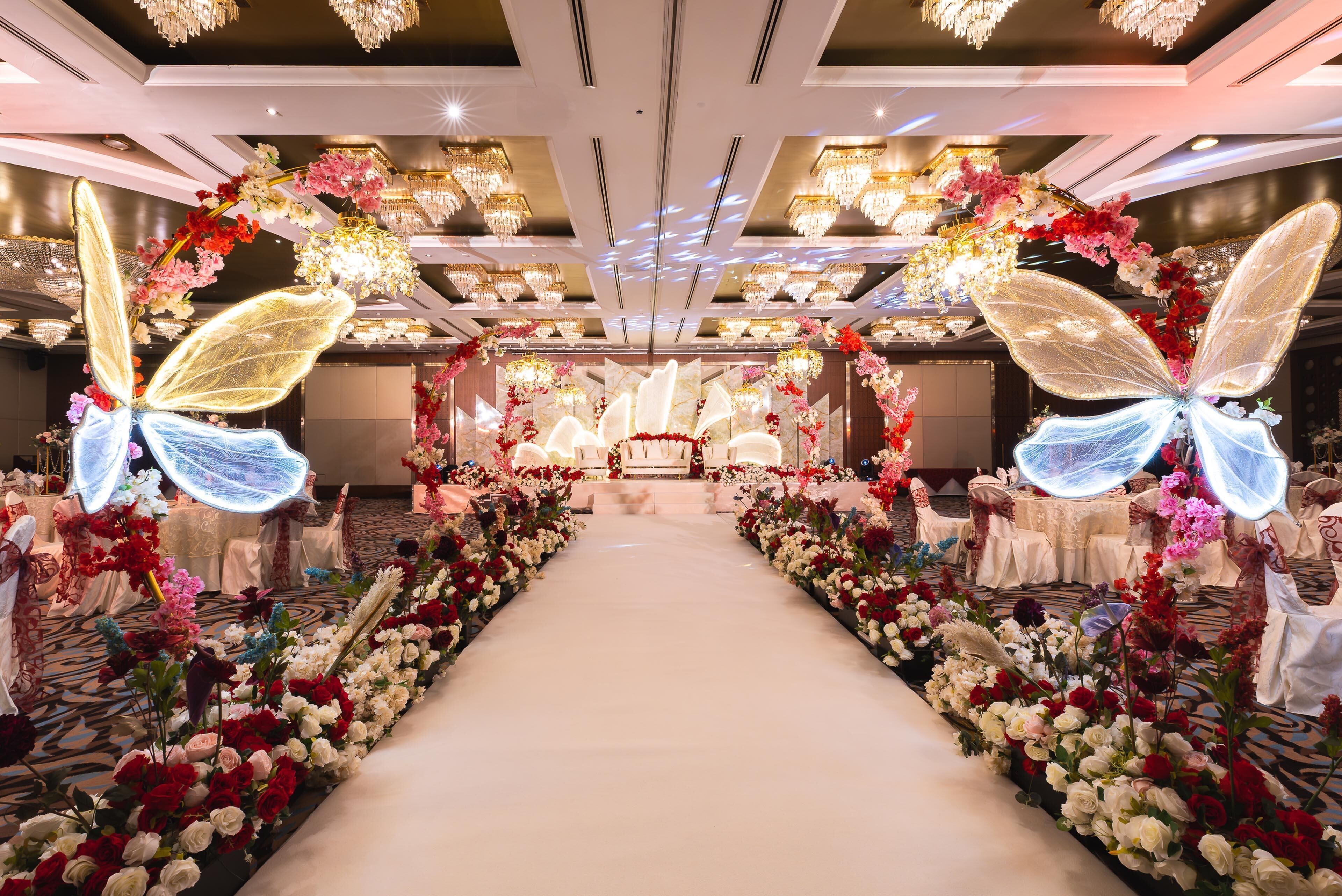 A hotel corridor with a floral aisle, chandeliers, and tables set for a banquet.