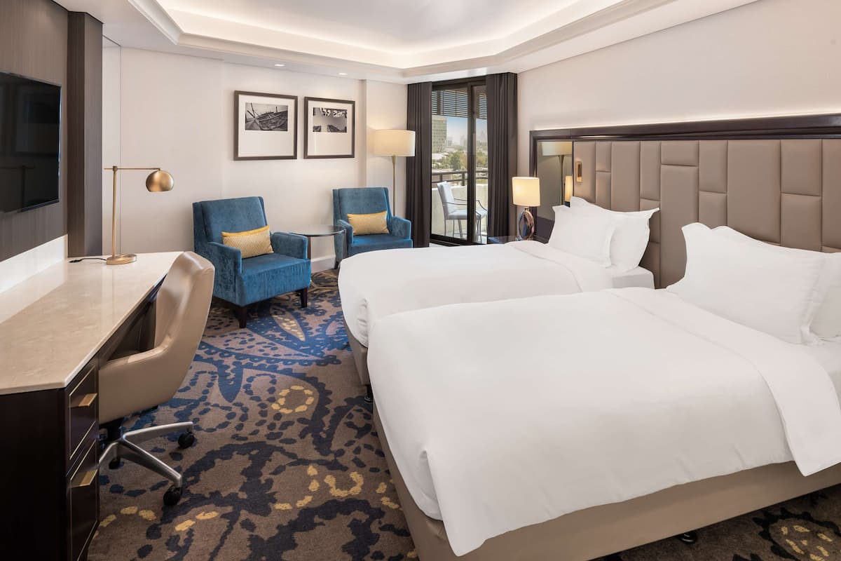 A hotel room with two beds, a desk, a chair, and a TV.