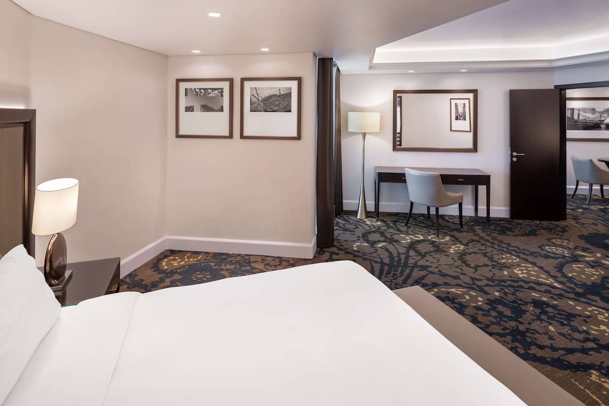 A hotel room with a bed, a desk, a chair, and a lamp.