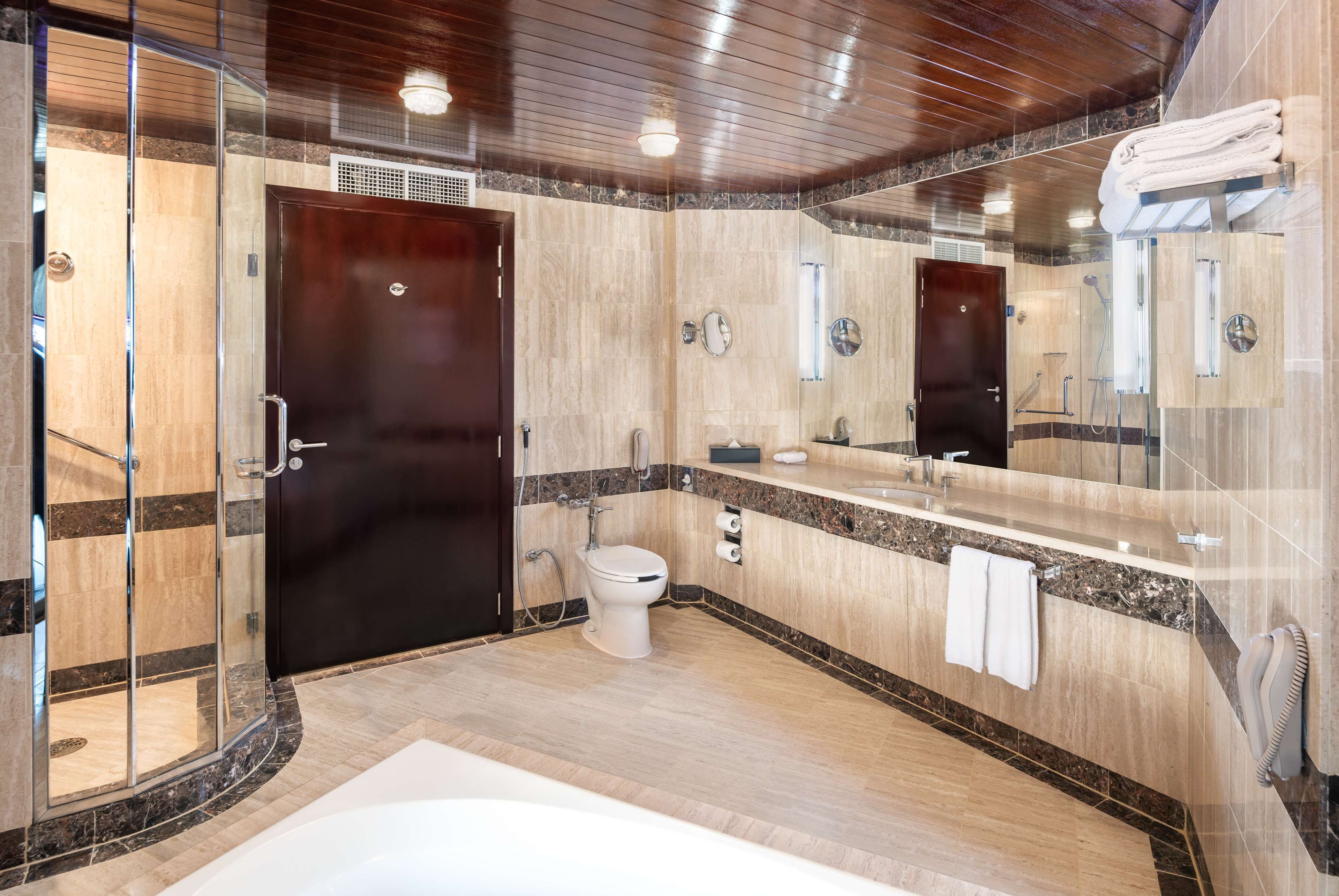 A modern bathroom with a glass shower enclosure, a large mirror, a bathtub, and a vanity with a sink and towel rack.
