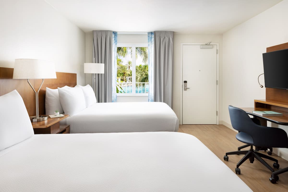 A hotel room with two beds, a desk with a chair, a TV, and a window with curtains.