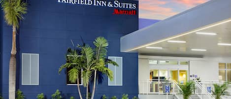 A Fairfield Inn & Suites Marriott hotel exterior with a modern design, palm trees, benches, and a clear sky.