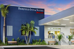 A Fairfield Inn & Suites Marriott hotel exterior with a modern design, palm trees, benches, and a clear sky.